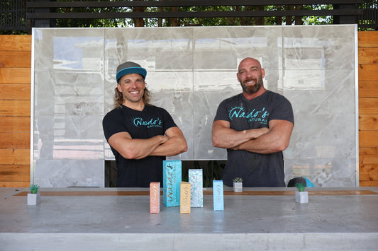 Danny and Kyle Nardo, Nardo's Natural founders smiling in front of skin care bottles on a counter top