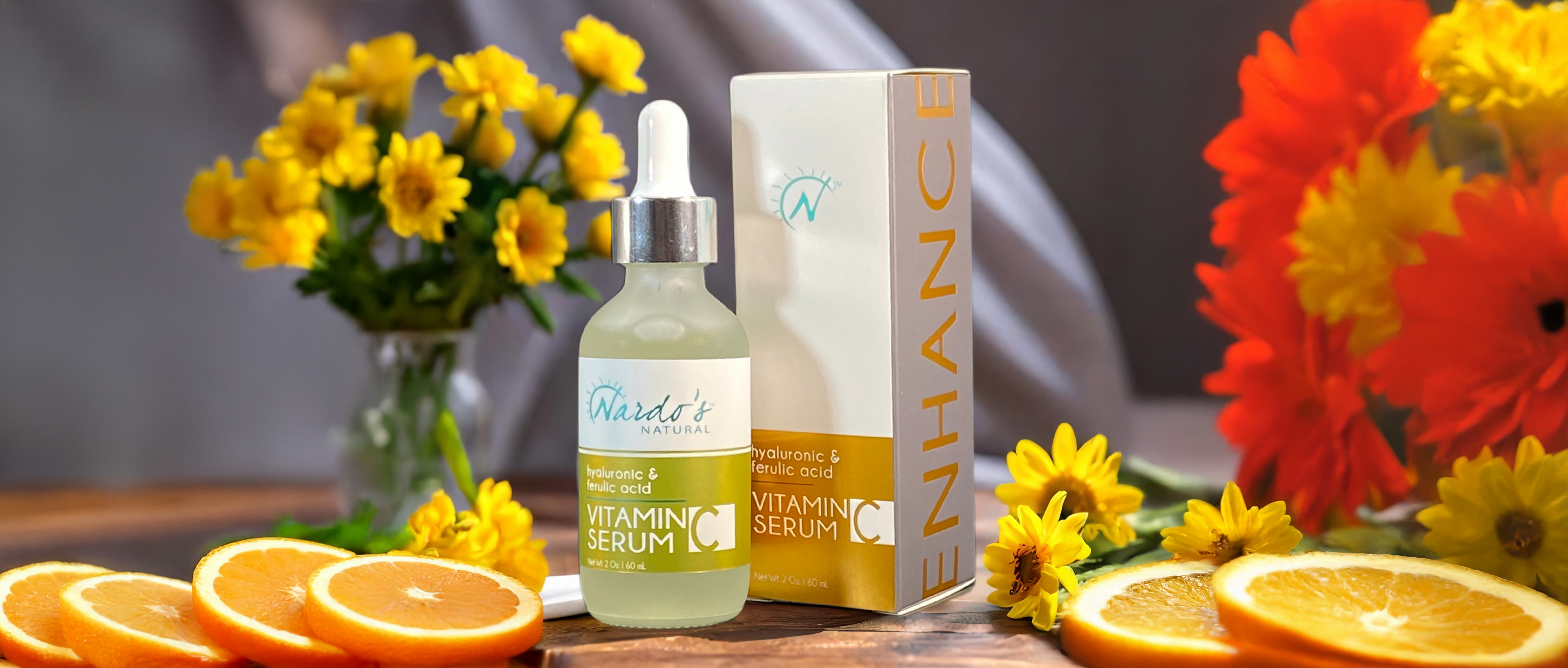 Vitamin serum bottle and box with flowers and oranges on a wooden surface